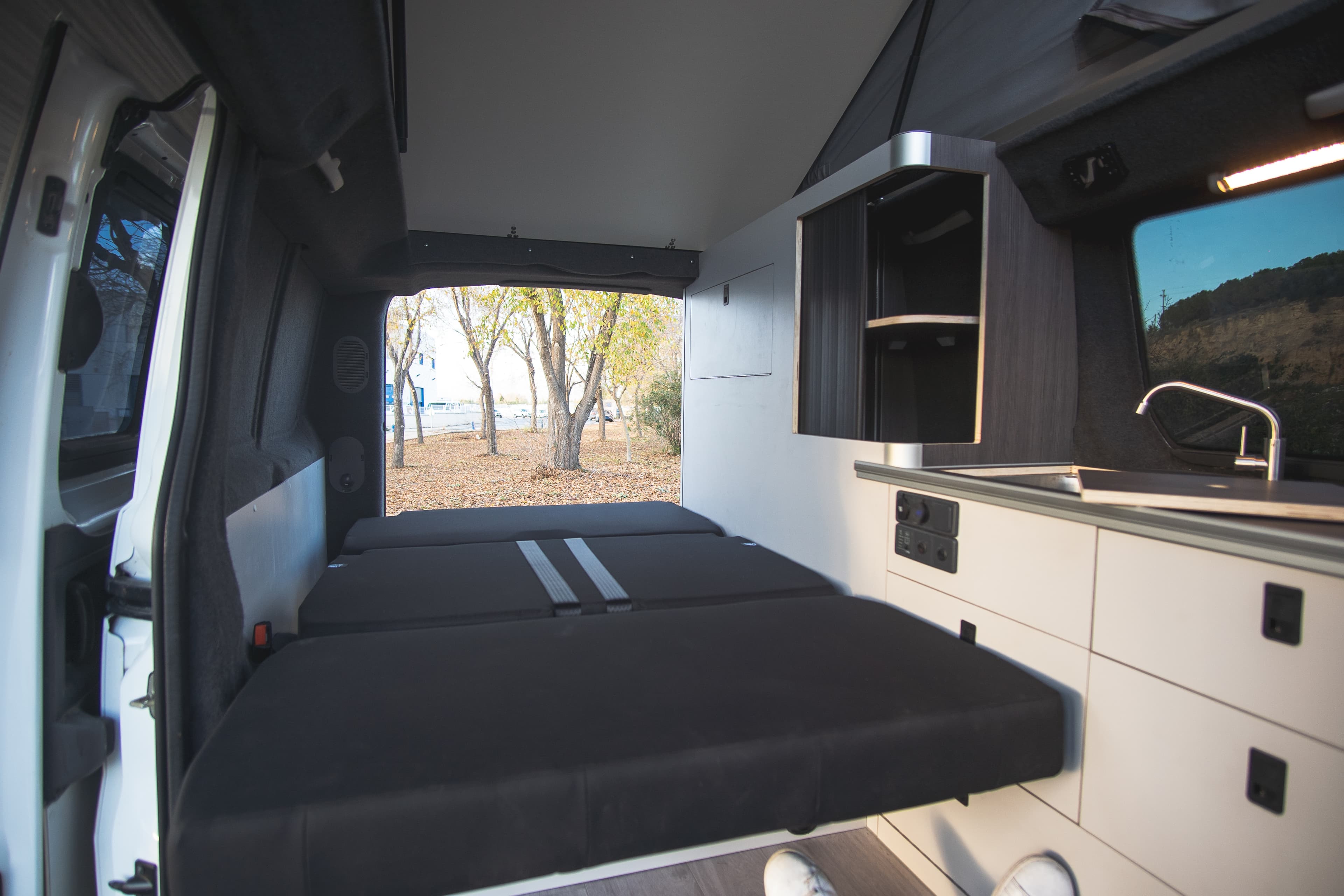 Interior de la camperización BILBAO con la cama desplegada y el techo elevable abierto